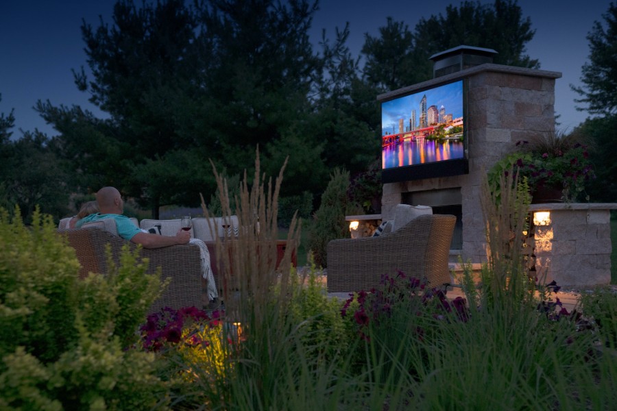 A person relaxing in a chair on a patio, enjoying an outdoor home theater.