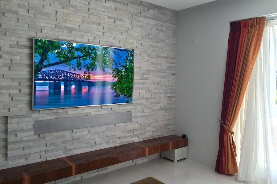 Architectural soundbar installed under a flat panel television to blend in with a brick wall.