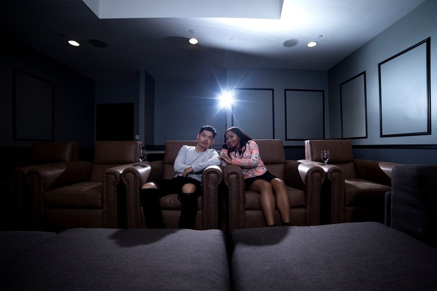 Two people lean toward one another on plush seating. A projector light shines above them.